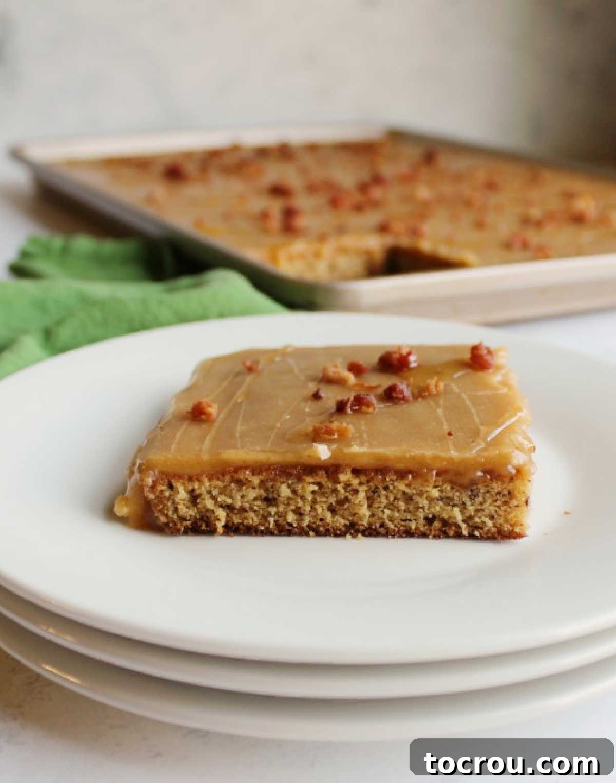 A perfectly portioned slice of banana sheet cake, topped with smooth peanut butter icing and visible bits of crispy bacon.