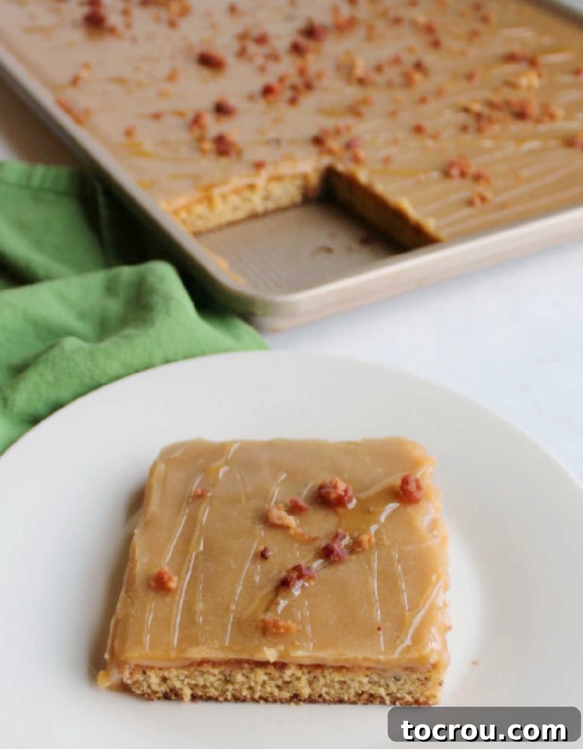 A slice of banana sheet cake with peanut butter icing and bacon bits on a dessert plate, with the remaining cake in the sheet pan in the background.