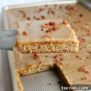 Close-up shot of the first slice of Elvis sheet cake being lifted from the pan, revealing the moist banana cake, smooth peanut butter icing, and crumbles of cooked bacon.