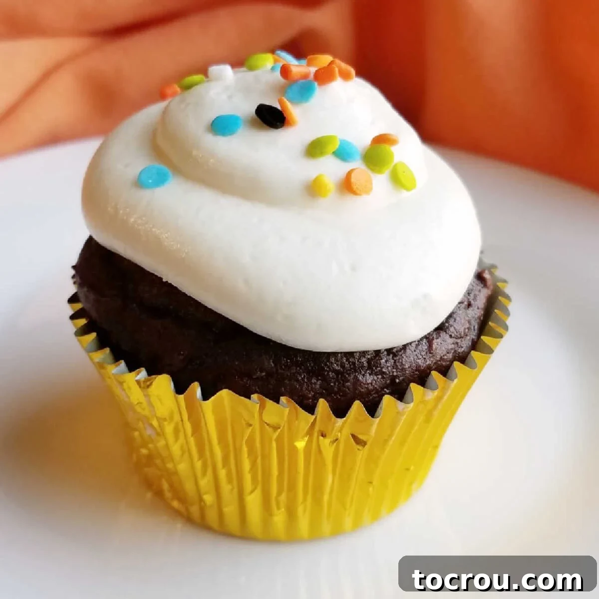 close up of chocolate pumpkin cupcake with frosting and sprinkles.