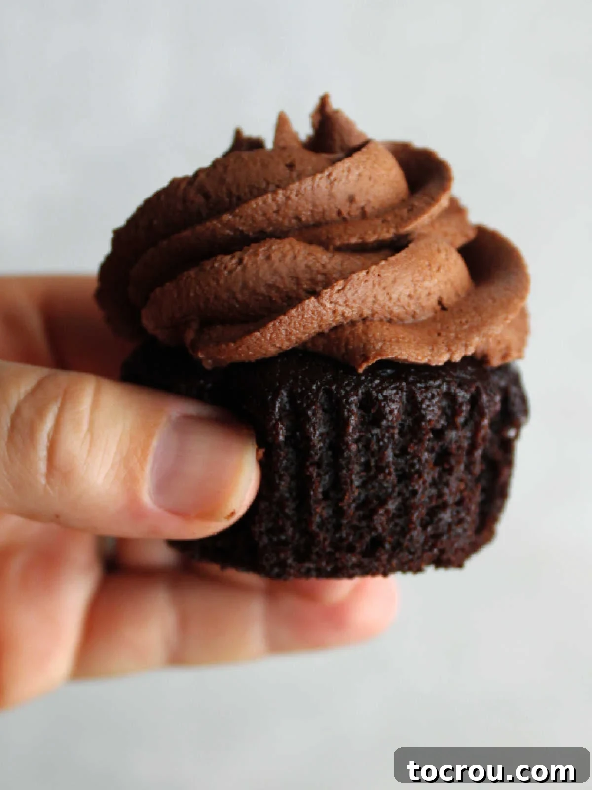 Hand holding a chocolate crazy cupcake topped with a swirl of ruffly chocolate condensed milk buttercream.