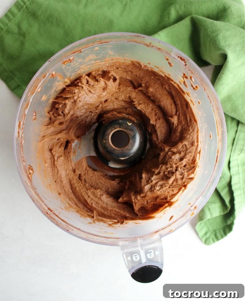 Blended Nice Cream in Food Processor The food processor bowl now shows a smooth, creamy blend of bananas, peanut butter, and chocolate, transformed into a rich nice cream texture.