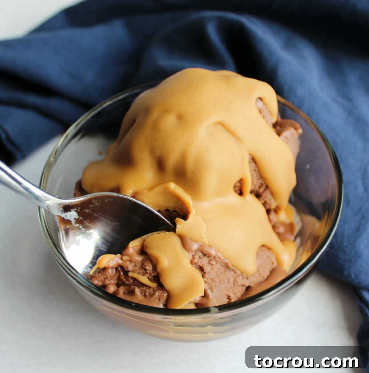 Nice Cream with Peanut Butter Magic Shell A bowl of chocolate peanut butter banana ice cream with a glistening peanut butter magic shell on top, presented on a blue napkin, inviting a delightful indulgence.