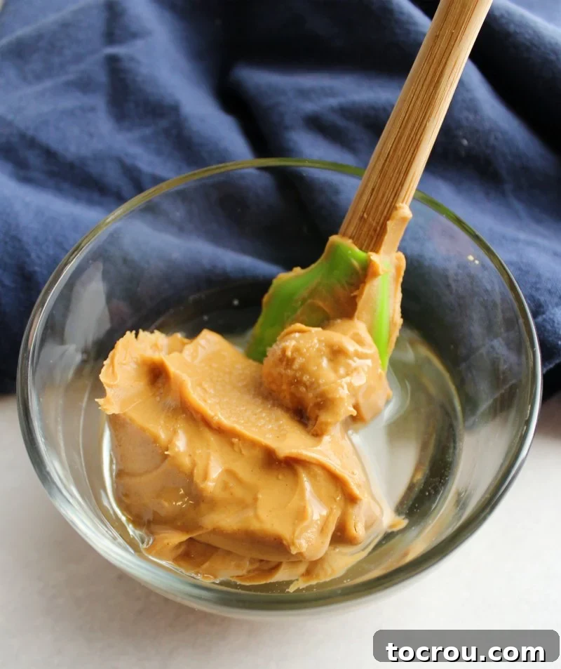 Small glass bowl with peanut butter and melted coconut oil, ready to be stirred.
