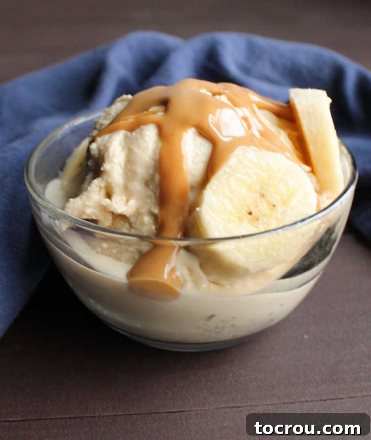 Glass bowl with ice cream, peanut butter magic shell, and banana slices, showcasing a delicious dessert.