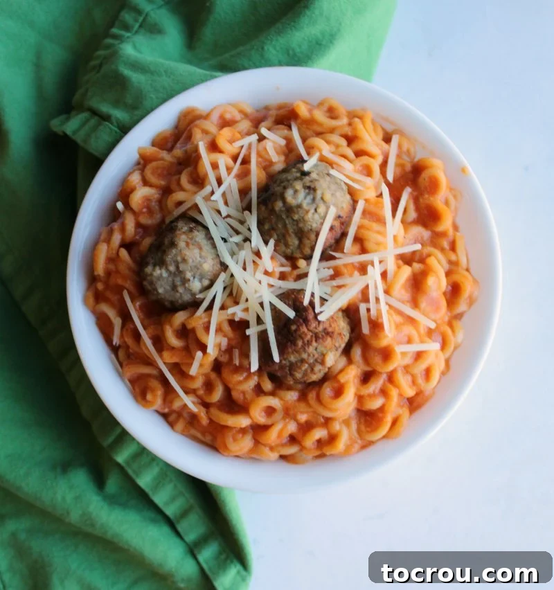 Hearty Homemade Spaghettios: The Ultimate Comfort Meal with Meatballs An inviting overhead shot showcasing a bowl of homemade Spaghettios, richly topped with savory meatballs and a generous sprinkle of melted cheese, emphasizing its comforting appeal.
