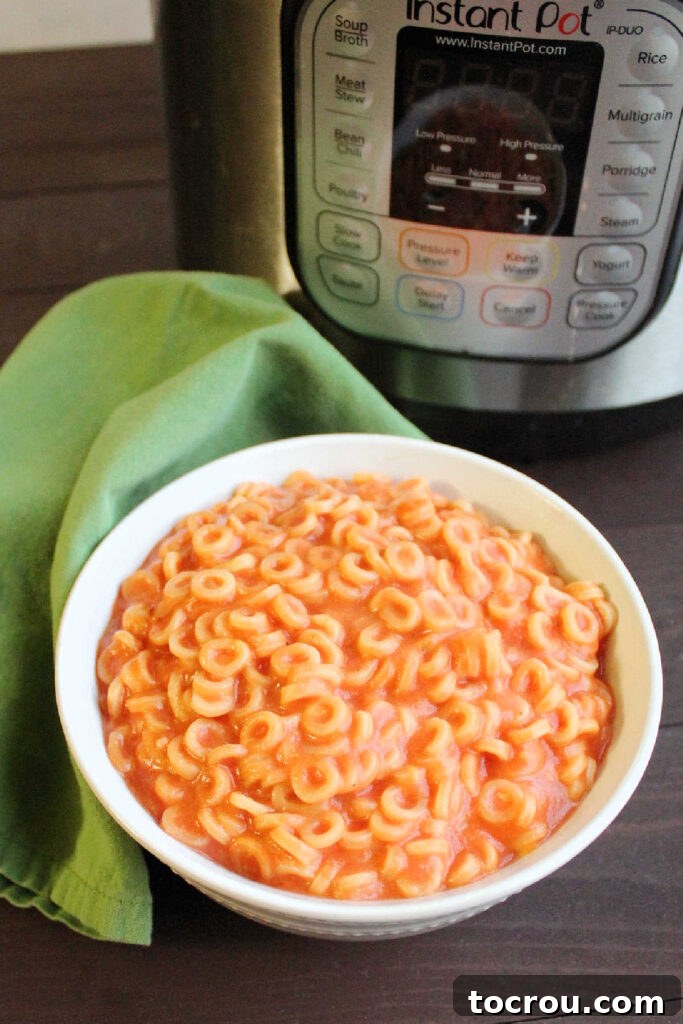 Quick & Cheesy: Instant Pot Spaghettios for an Effortless Meal A vibrant overhead view of a bowl of cheesy tomato Spaghettios, perfectly cooked and glistening, positioned in front of a pressure cooker, highlighting the ease of preparation.