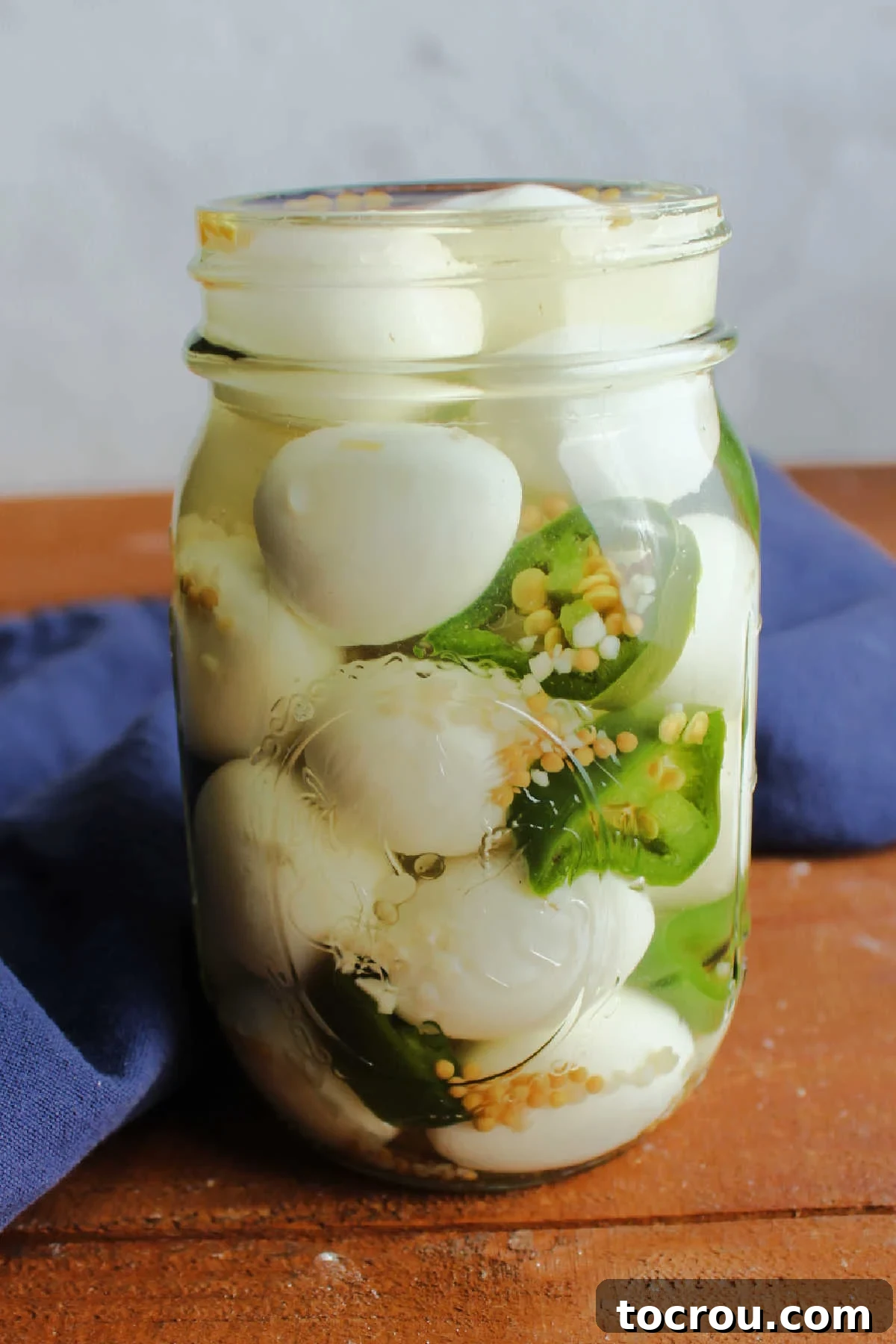 Jar of spicy pickled quail eggs with sliced jalapenos, a flavorful snack.