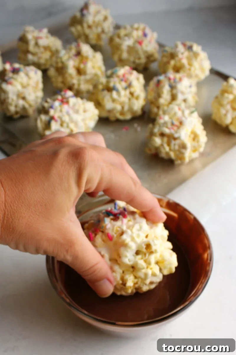 Marshmallowy Popcorn Delights 7 hand dunking marshmallow popcorn ball into bowl of melted milk chocolate.