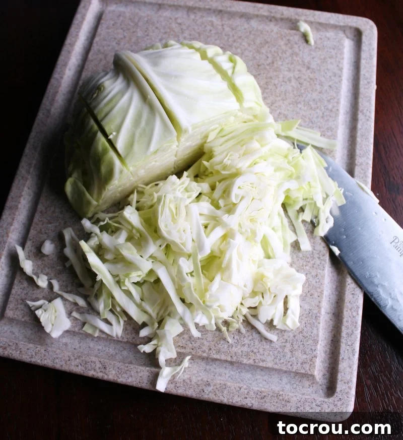 Head of cabbage on a cutting board being cut into small pieces for coleslaw.