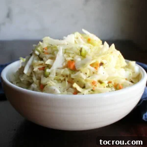 Close up of a white serving bowl loaded with tangy vinegar based coleslaw.