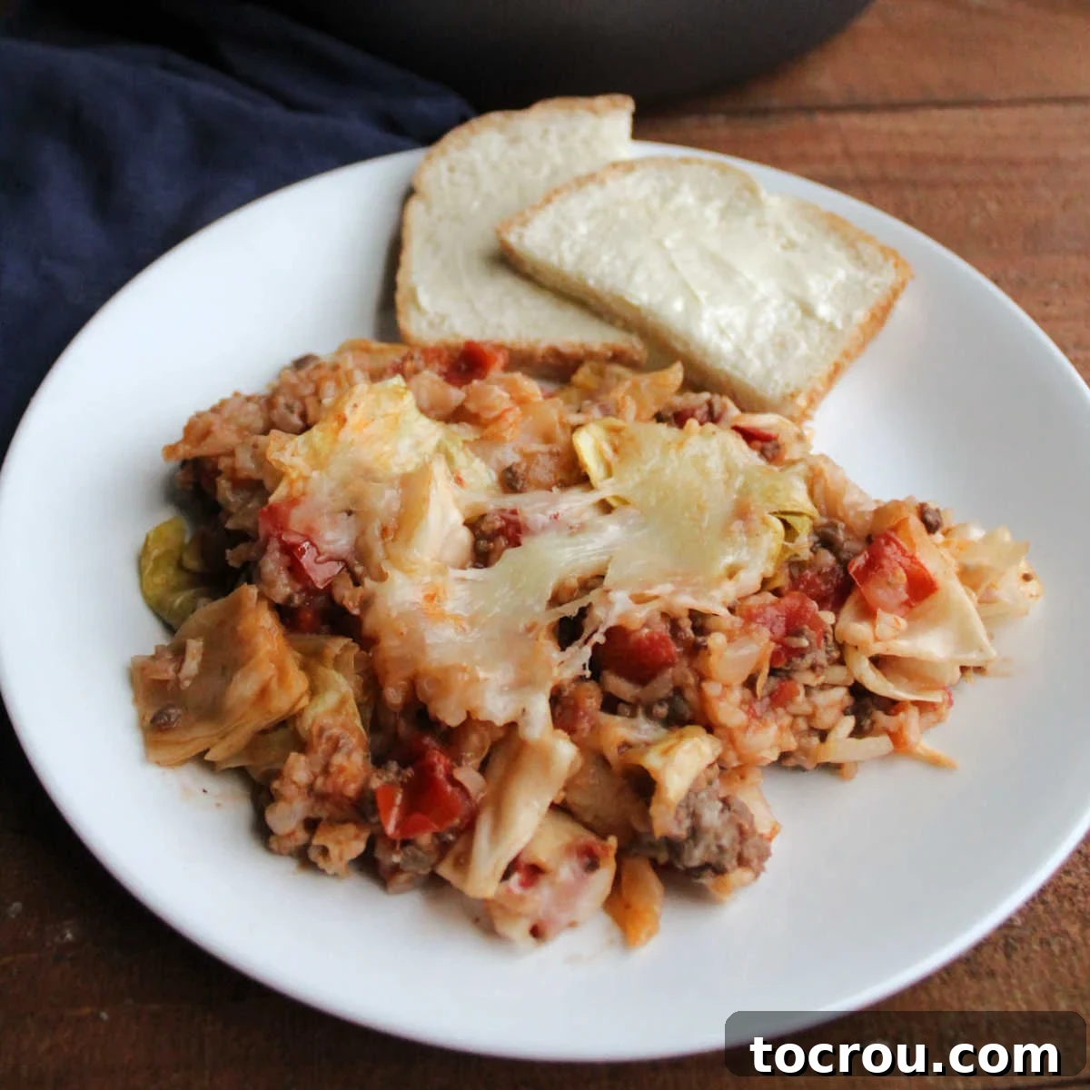 Plate of unstuffed cabbage roll skillet meal topped with melted cheese and served with buttered bread, showcasing a delicious and easy one-pan dinner.