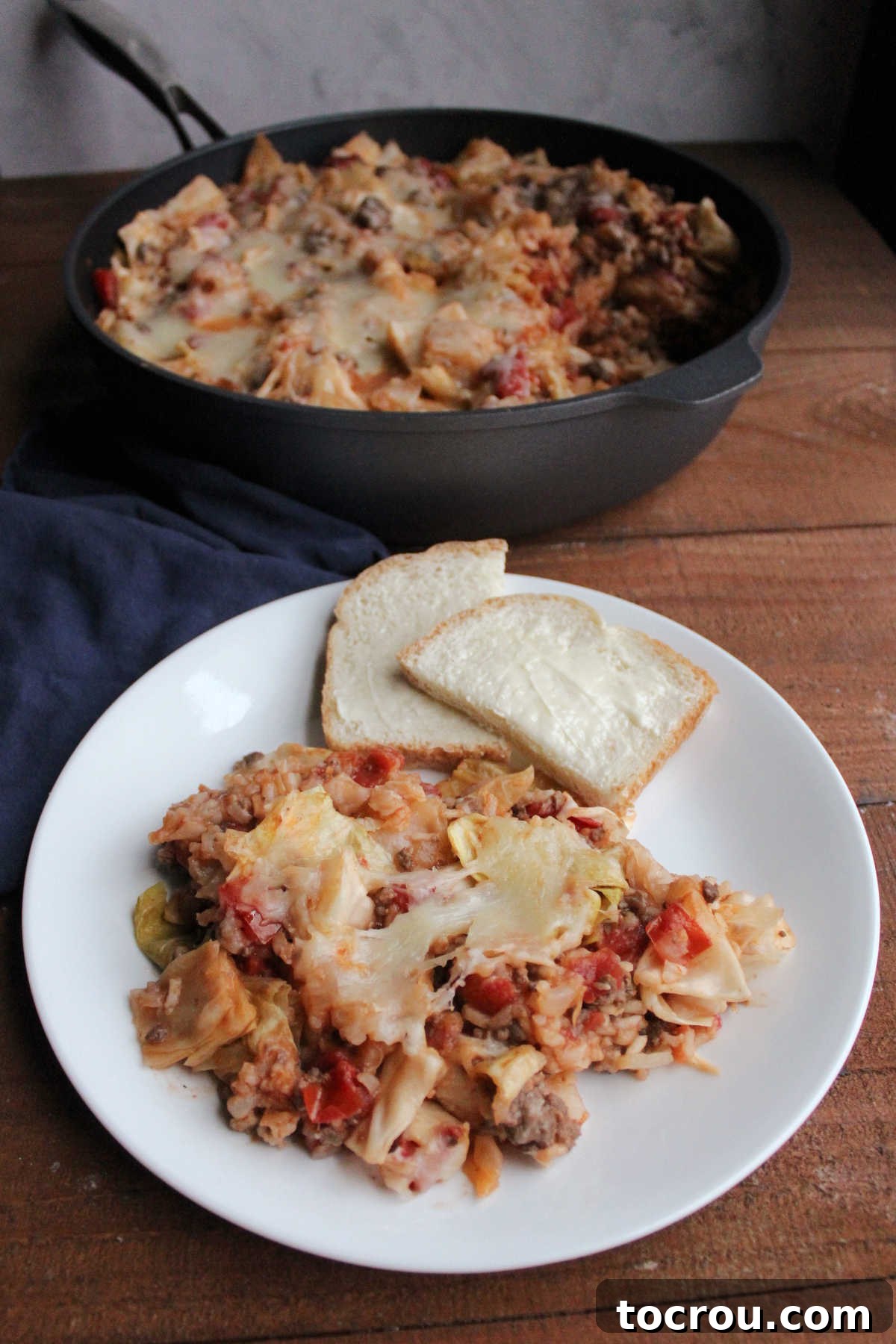 A serving of unstuffed cabbage roll skillet meal on a white plate, with the skillet of remaining meal in the background, ready to be enjoyed.