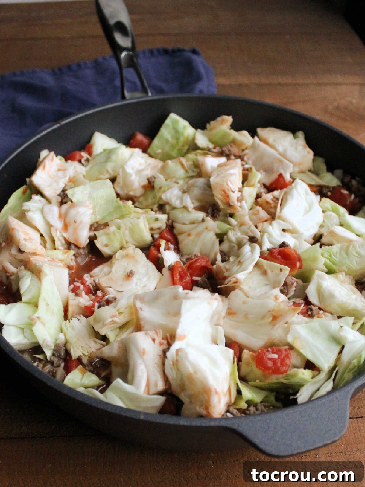 Large sauté pan filled with a vibrant mixture of chopped cabbage, uncooked rice, diced tomatoes, and other ingredients, just before cooking.