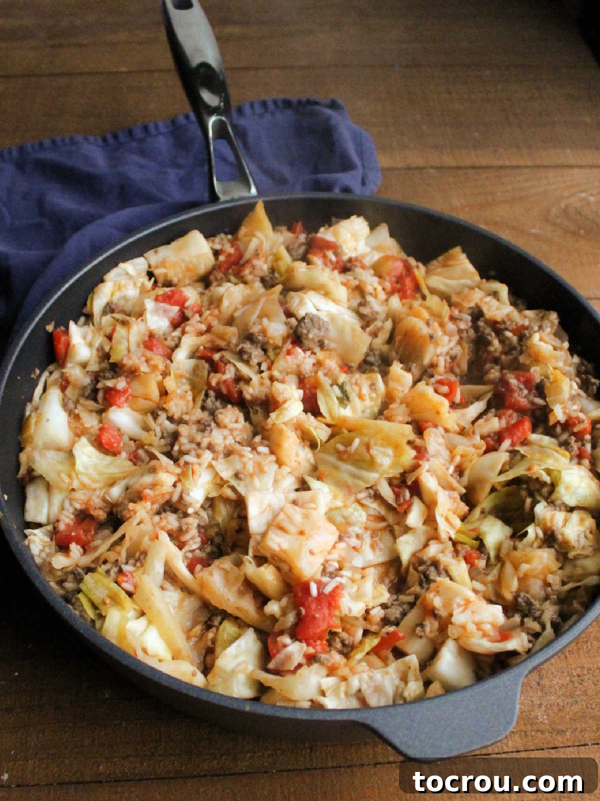 Cooked cabbage, rice, ground beef, and tomato sauce mixture simmering in a skillet, ready to be topped with cheese for a cheesy unstuffed cabbage roll skillet meal.
