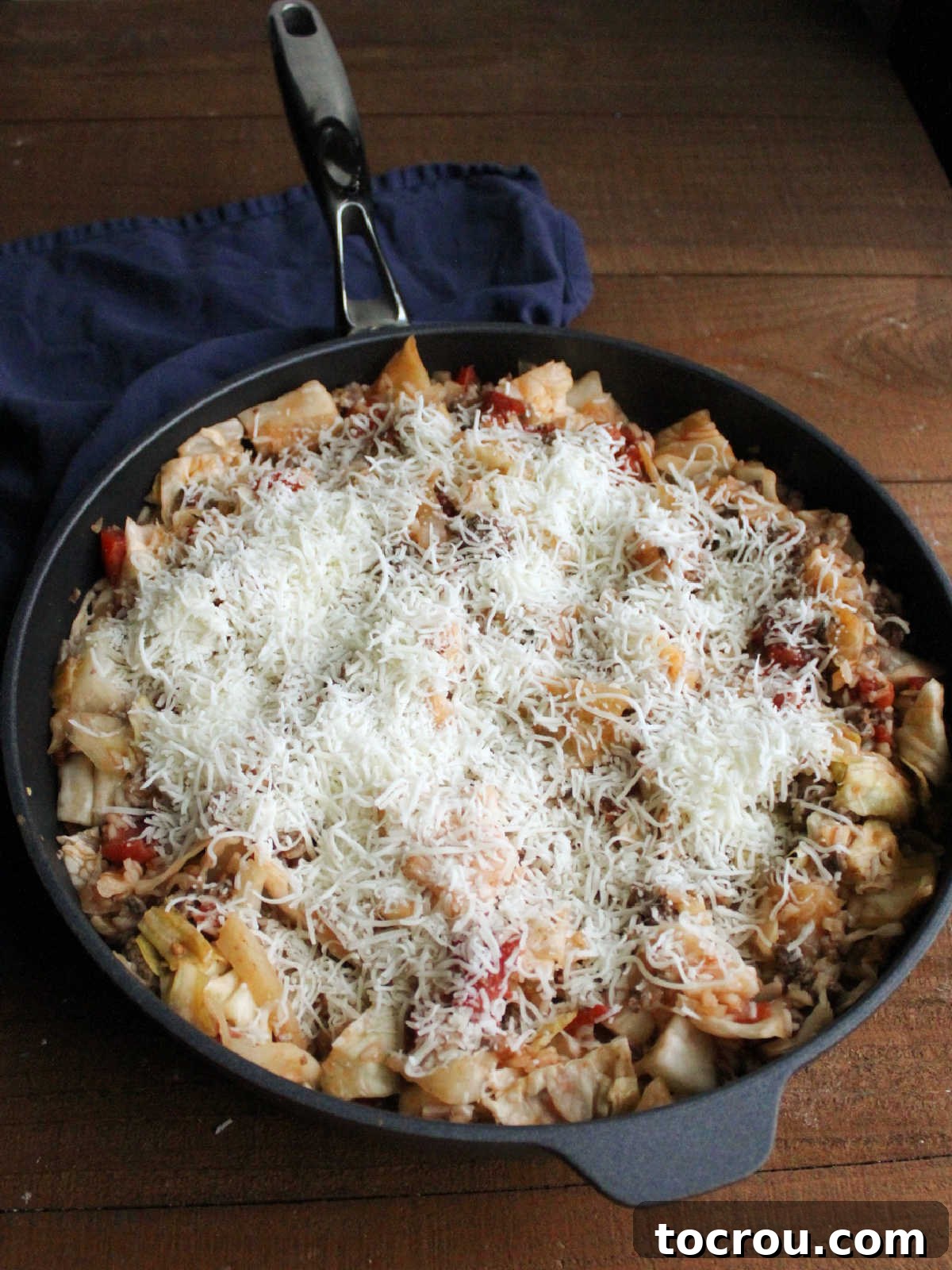 Finely shredded mozzarella cheese being sprinkled generously over the cooked unstuffed cabbage roll skillet mixture, preparing it for melting.