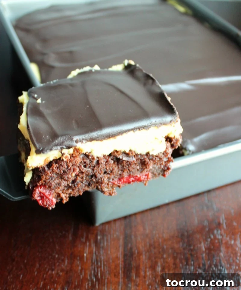 Decadent Black Forest Sheet Cake 6 Lifting the first slice of cake from the pan, revealing moist chocolate cake with cherries, a creamy vanilla layer, and rich chocolate topping.