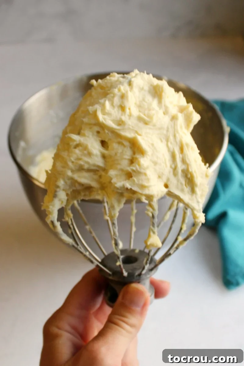 Fluffy Vanilla German Buttercream Hand holding a mixer beater full of custardy German buttercream, rich and ready to be used on a cake.
