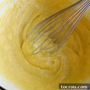 Slightly lumpy custard mixture in pan with whisk, ready to be beaten smooth.