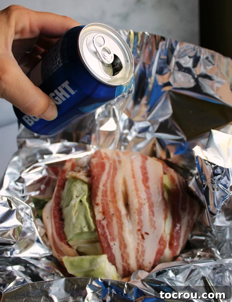 Beer Braised Cabbage Wrapped in Bacon 4 pouring beer over bacon wrapped head of cabbage in foil bowl.