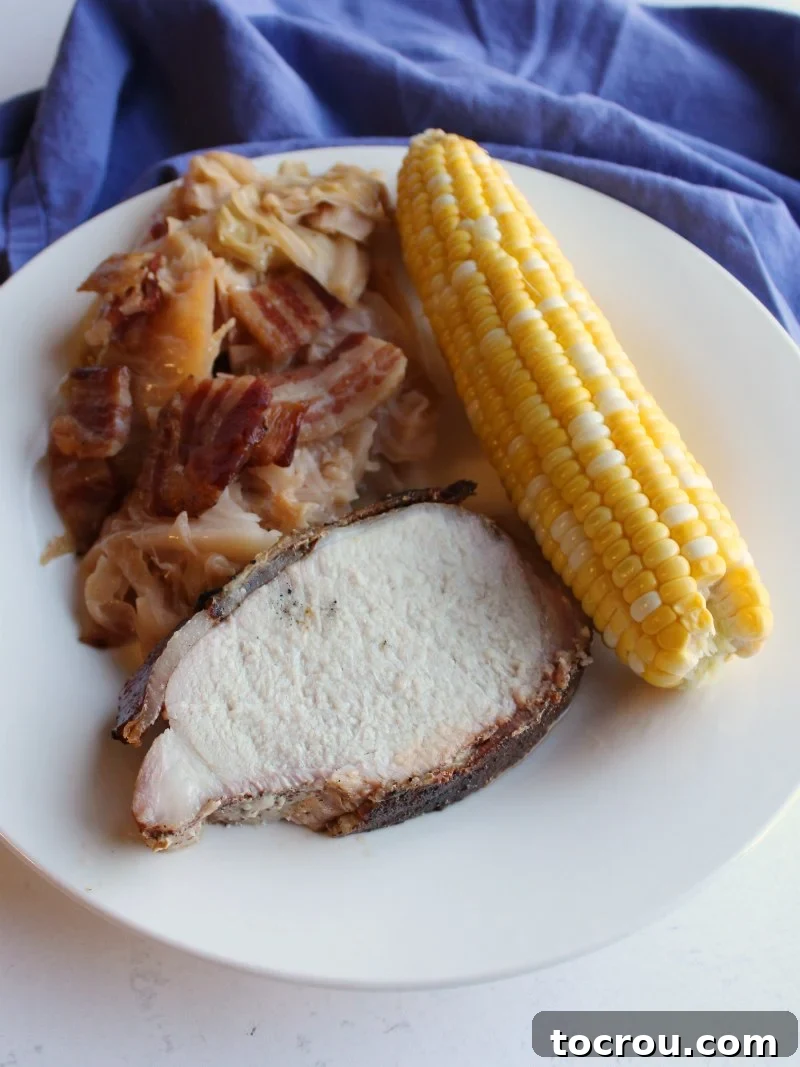 A whole head of cabbage wrapped in bacon and braised in beer is a thing of glory. Make it on the grill or in the oven for a flavorful side dish. dinner plate with pork, bacon wrapped cabbage and corn on the cob all done on the grill.