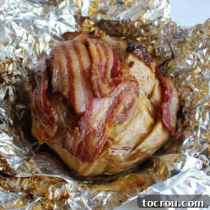 whole head of cabbage wrapped in bacon fresh off the grill and partially wrapped in foil.