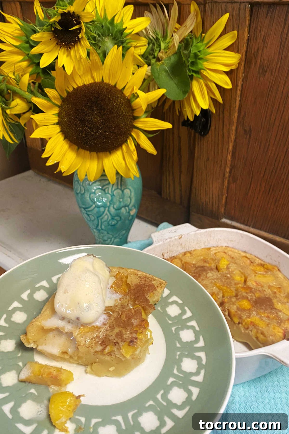 Peach Clafoutis with Ice Cream A slice of warm peach clafoutis served on a plate with a scoop of creamy butter pecan ice cream.