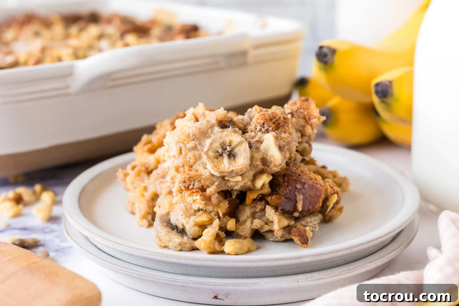 A generous serving of golden-brown banana bread pudding, adorned with crunchy walnuts and drizzled with a rich, sweet condensed milk sauce, perfectly baked and ready to be enjoyed.