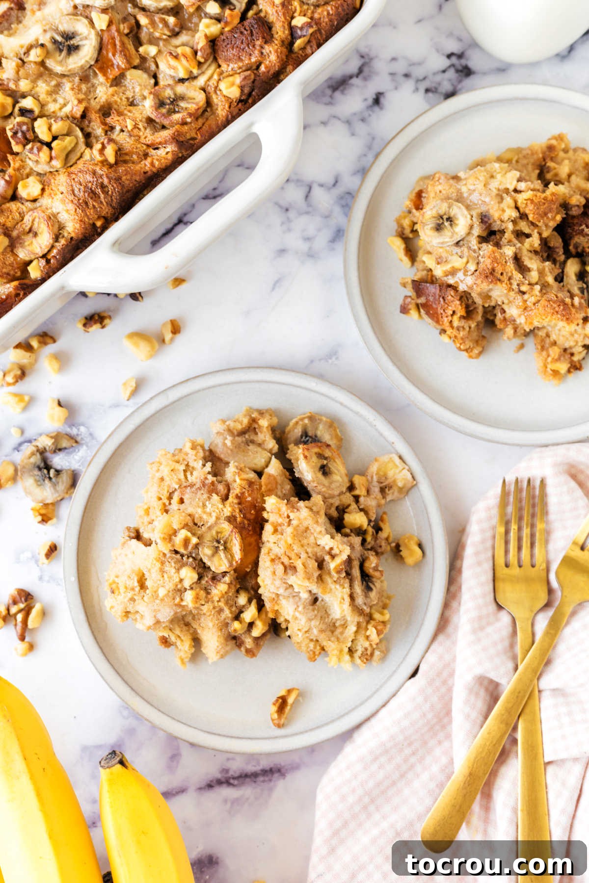 Two exquisitely prepared servings of banana bread pudding, artfully plated on dessert dishes with forks resting nearby, inviting diners to indulge in this comforting and visually appealing treat.