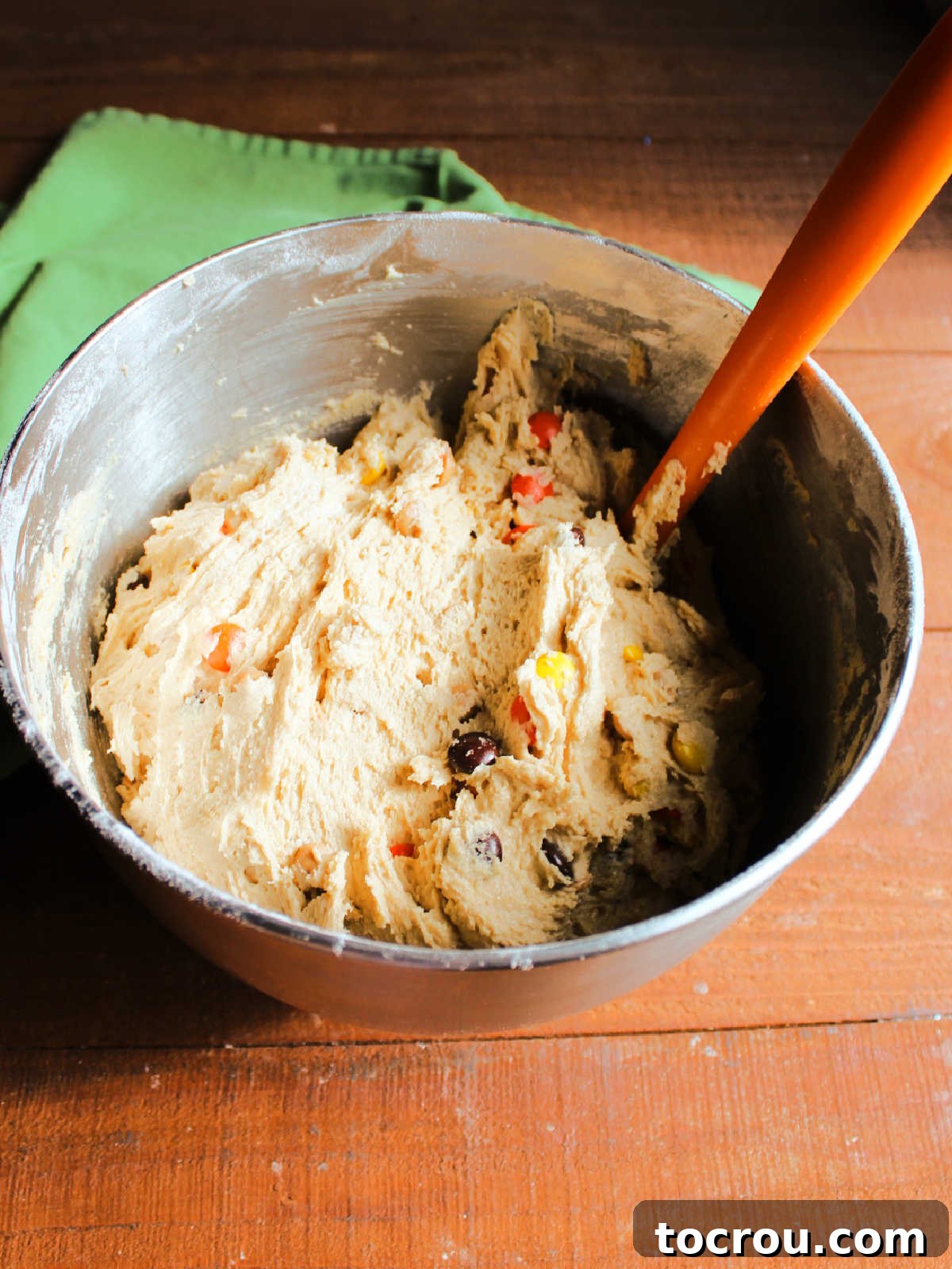 Rich peanut butter cookie dough, generously studded with golden peanut butter chips and colorful Reese's Pieces candies, mixed and ready for chilling.