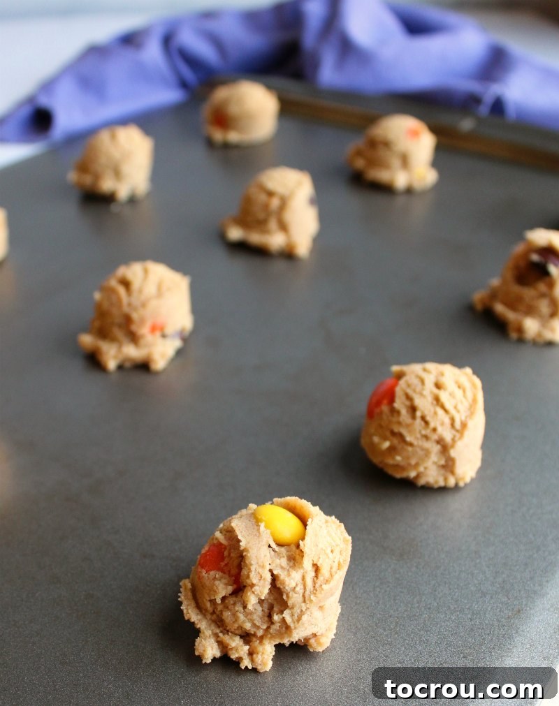 Perfectly portioned balls of triple peanut butter cookie dough, neatly arranged on a baking sheet, awaiting their delicious transformation in the oven.