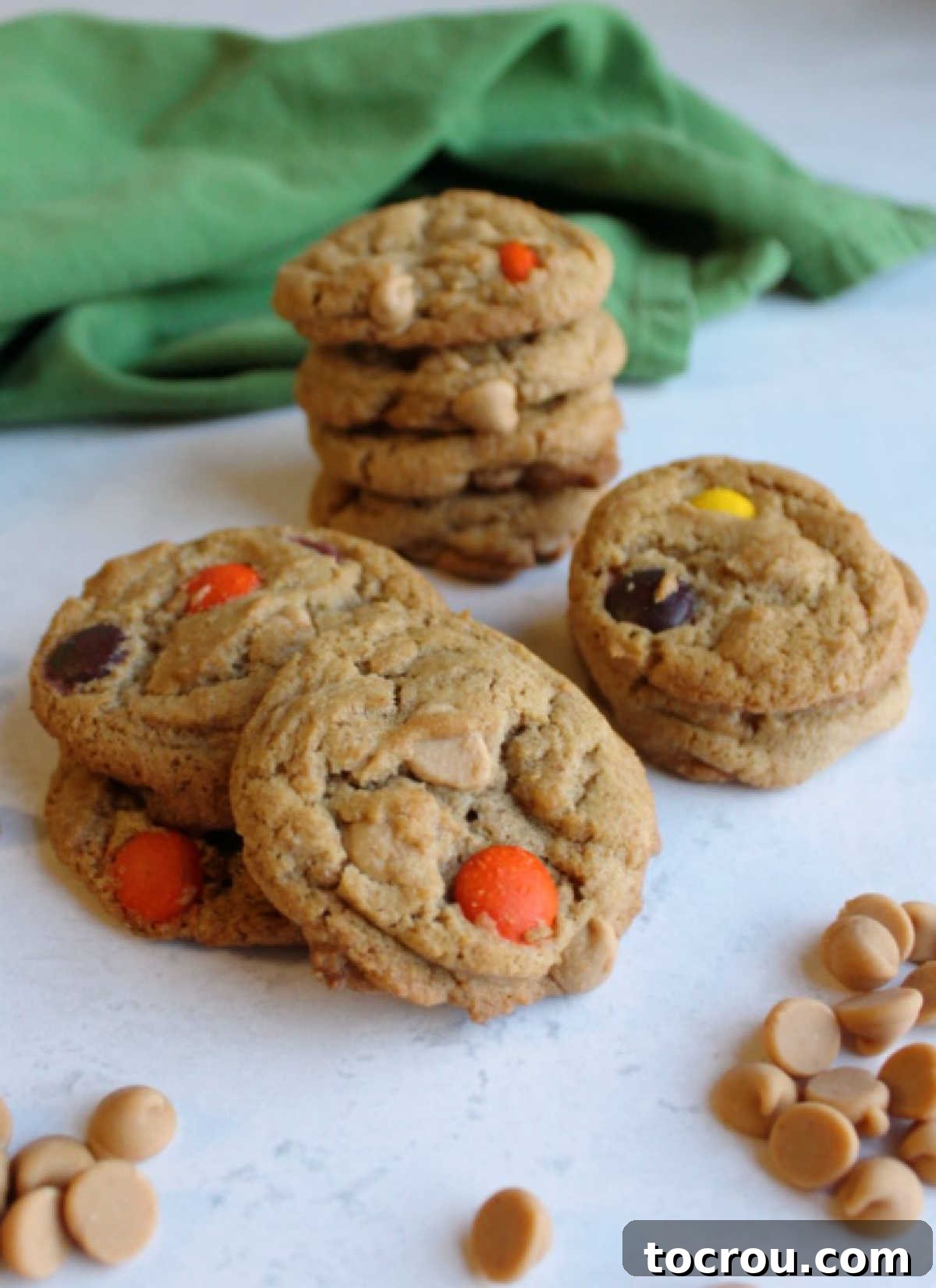 Neatly stacked piles of golden brown triple peanut butter cookies, each bursting with peanut butter chips, positioned next to a bowl of extra peanut butter chips, ready to be enjoyed.