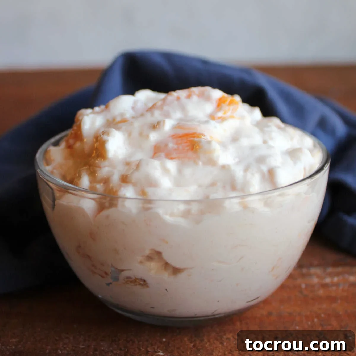 Small glass bowl with a serving of creamy orange jello salad with cottage cheese and pineapple, ready to eat.