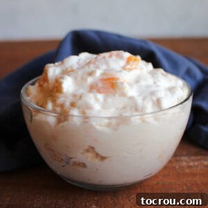 Small glass bowl with a serving of creamy orange jello salad with cottage cheese and pineapple, ready to eat.