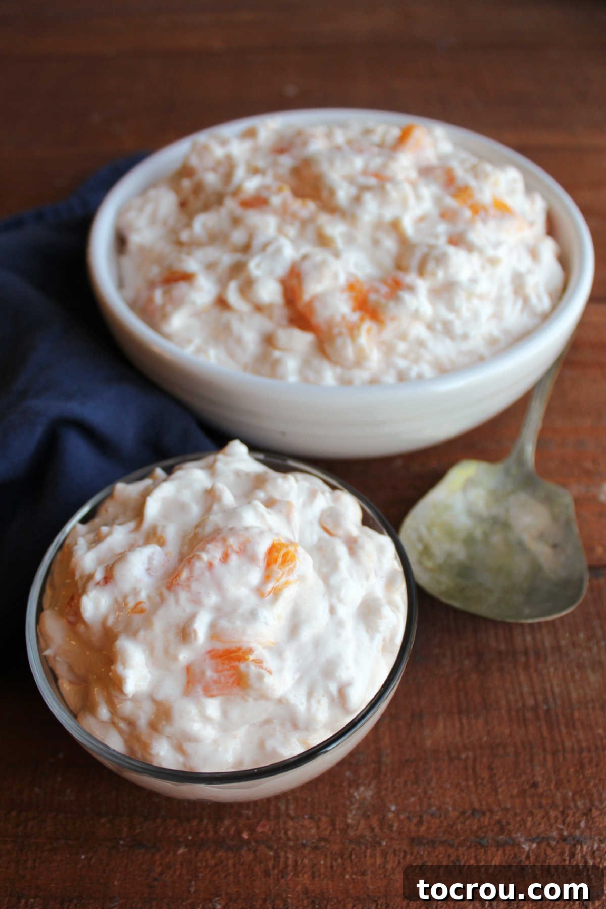 Small glass bowl of orange jello salad in front of larger white serving bowl with more cottage cheese jello salad inside. 