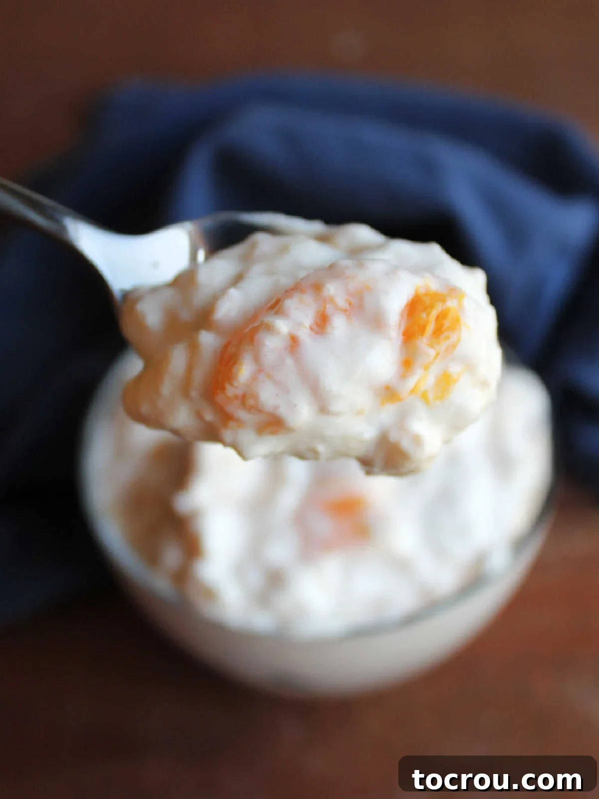Small spoon with a bite of orange cottage cheese jello salad on it, showing creamy texture and bits of fruit.