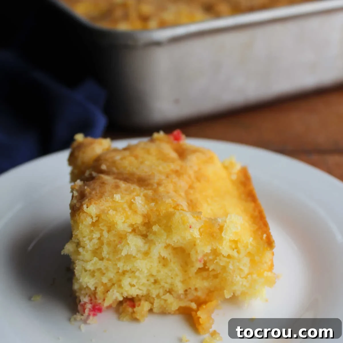 A beautiful slice of fluffy fruit cocktail cake with a moist, tender crumb and visible pieces of vibrant fruit, perfectly placed on a plate, ready to be enjoyed.