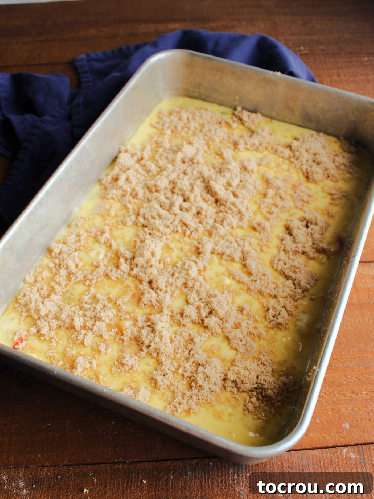 Fruit cocktail cake batter evenly spread in a 9x13-inch baking pan, generously topped with light brown sugar, poised to enter the oven.