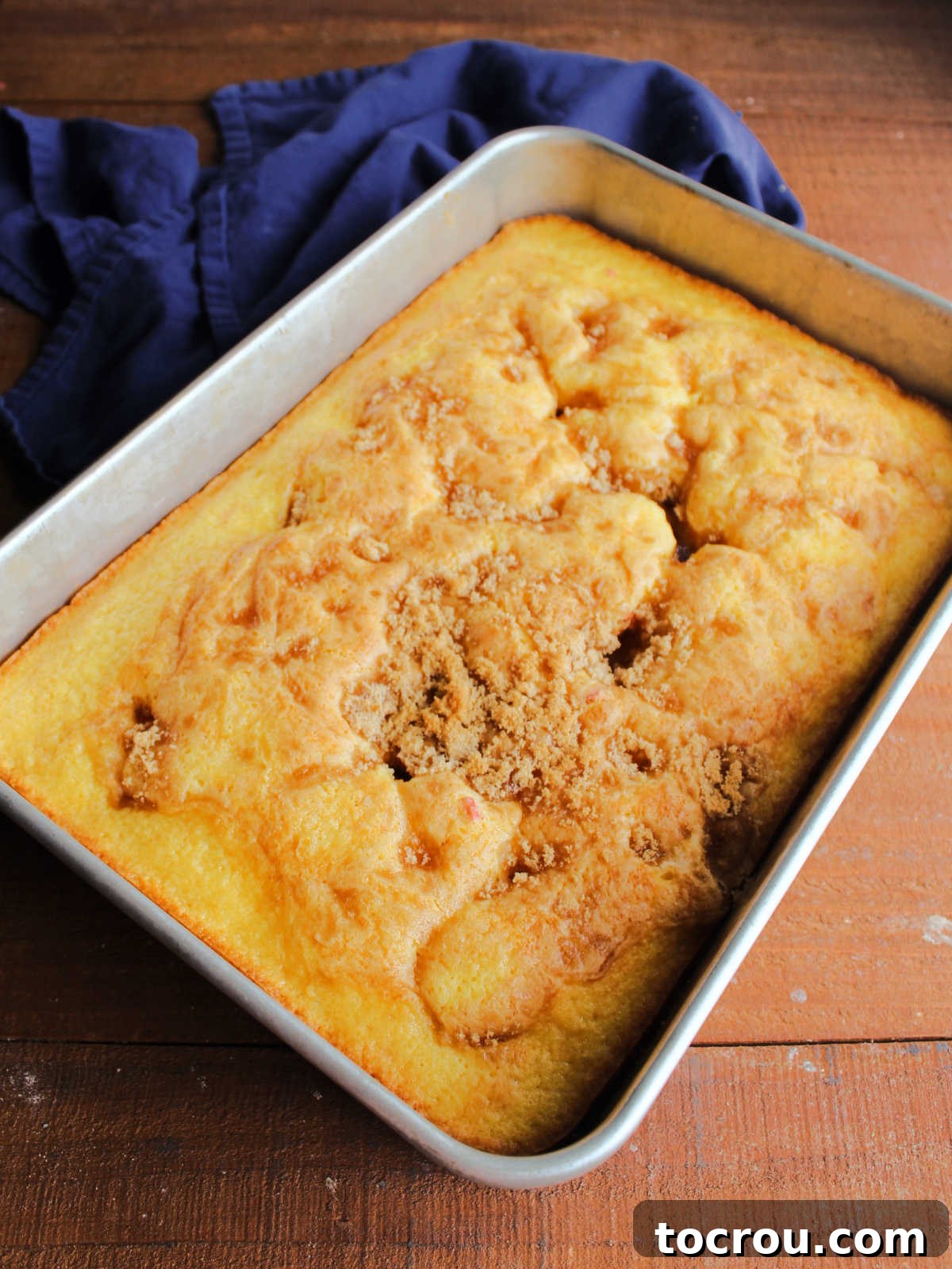 A freshly baked fruit cocktail cake made with a cake mix, showcasing a beautifully golden brown sugar topping, cooling in its pan.