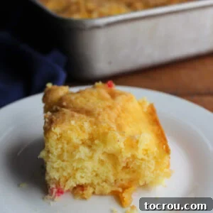 Piece of fluffy fruit cocktail cake with moist crumb and bits of fruit on a plate, ready to eat.