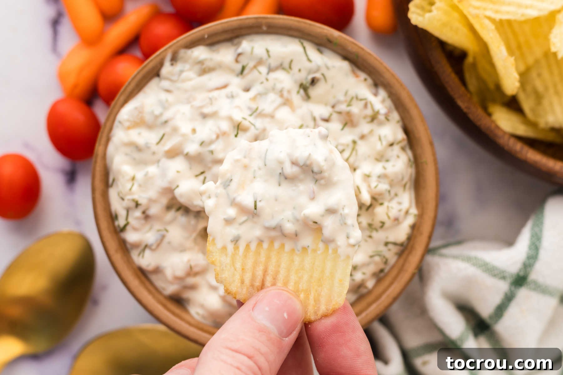 Irresistible Homemade Caramelized Onion Dip with Potato Chips Hand holding ruffled potato chip with homemade onion dip on it, ready to eat.