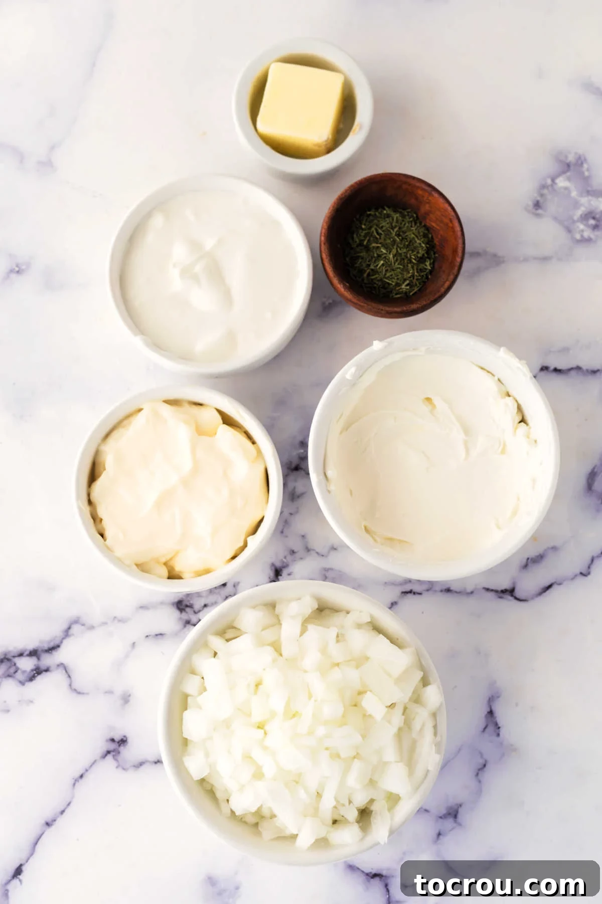 Essential Ingredients for Creamy Caramelized Onion Dip Ingredients including diced onion, butter, sour cream, mayonnaise, cream cheese, and dill ready to be made into a cold chip dip.