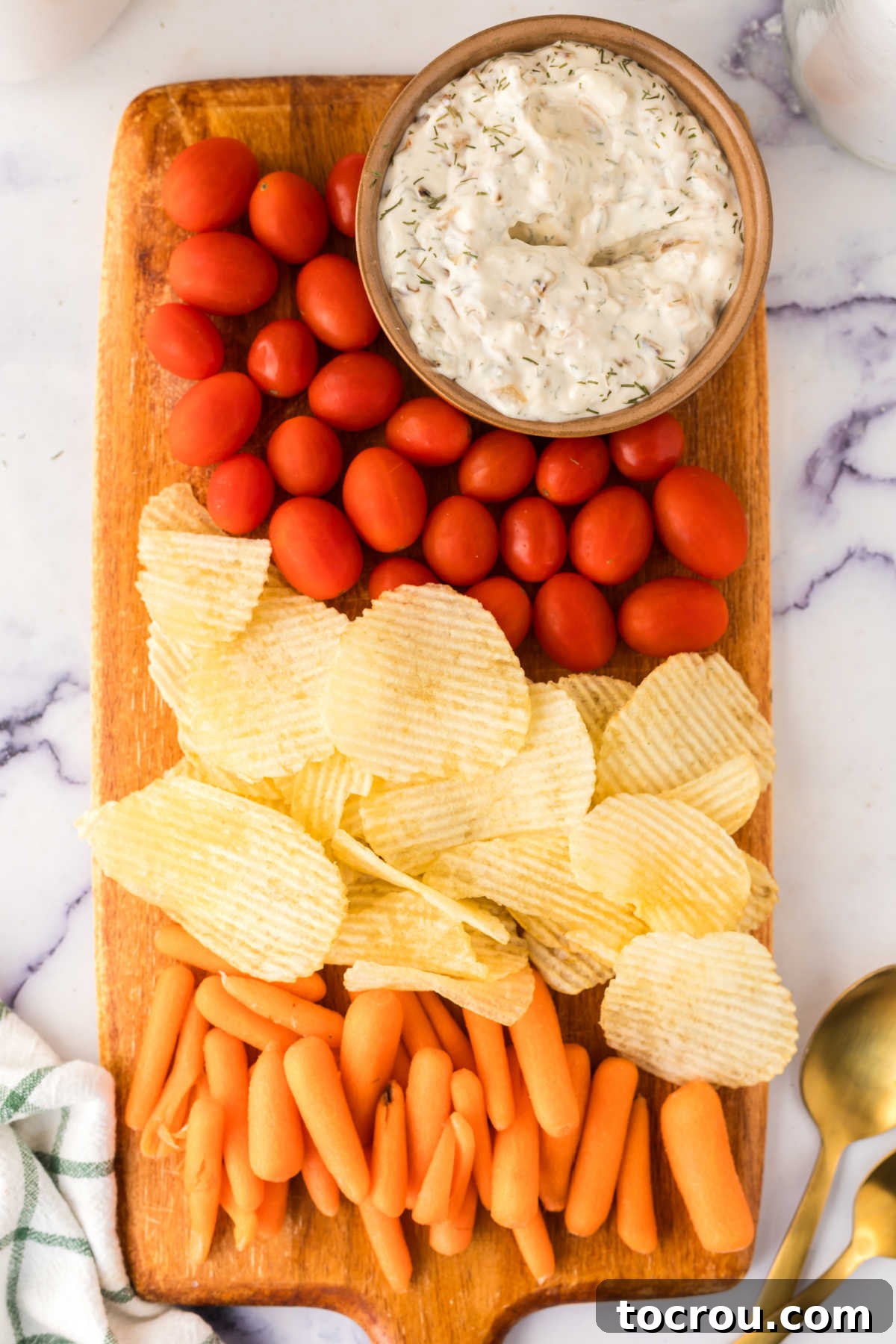 Caramelized Onion Dip Featured on a Festive Snack Board Snack board with bowl of caramelized onion dip, cherry tomatoes, potato chips, and baby carrots.