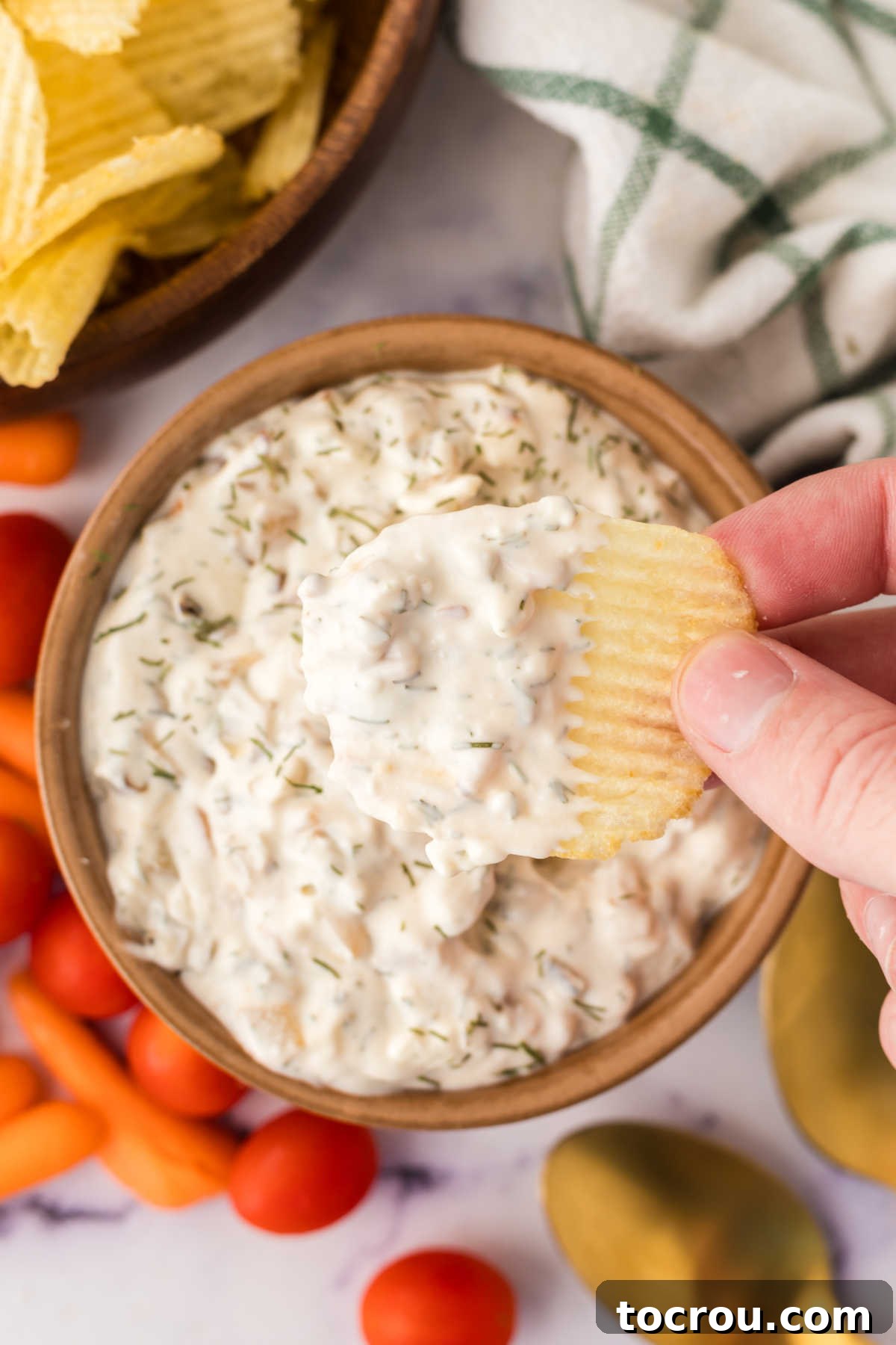 Savoring a Bite of Homemade Caramelized Onion Dip Hand holding ruffled potato chip with creamy onion dip on it, ready to eat.