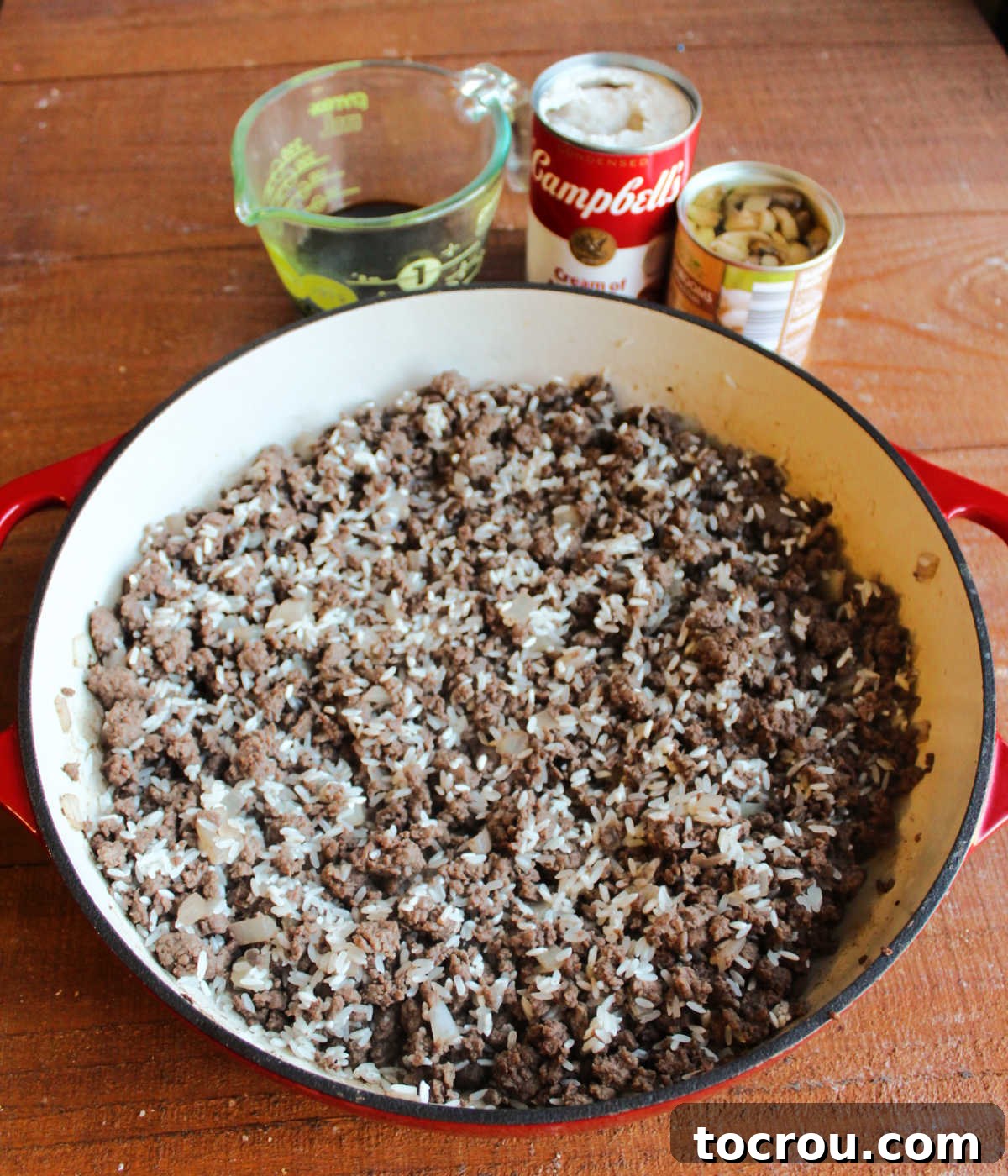 Hearty Creamy Venison Mushroom Rice 5 Pan of browned ground venison with toasted rice next to measuring cup of soy sauce, can of cream of mushroom, and can of sliced mushrooms.