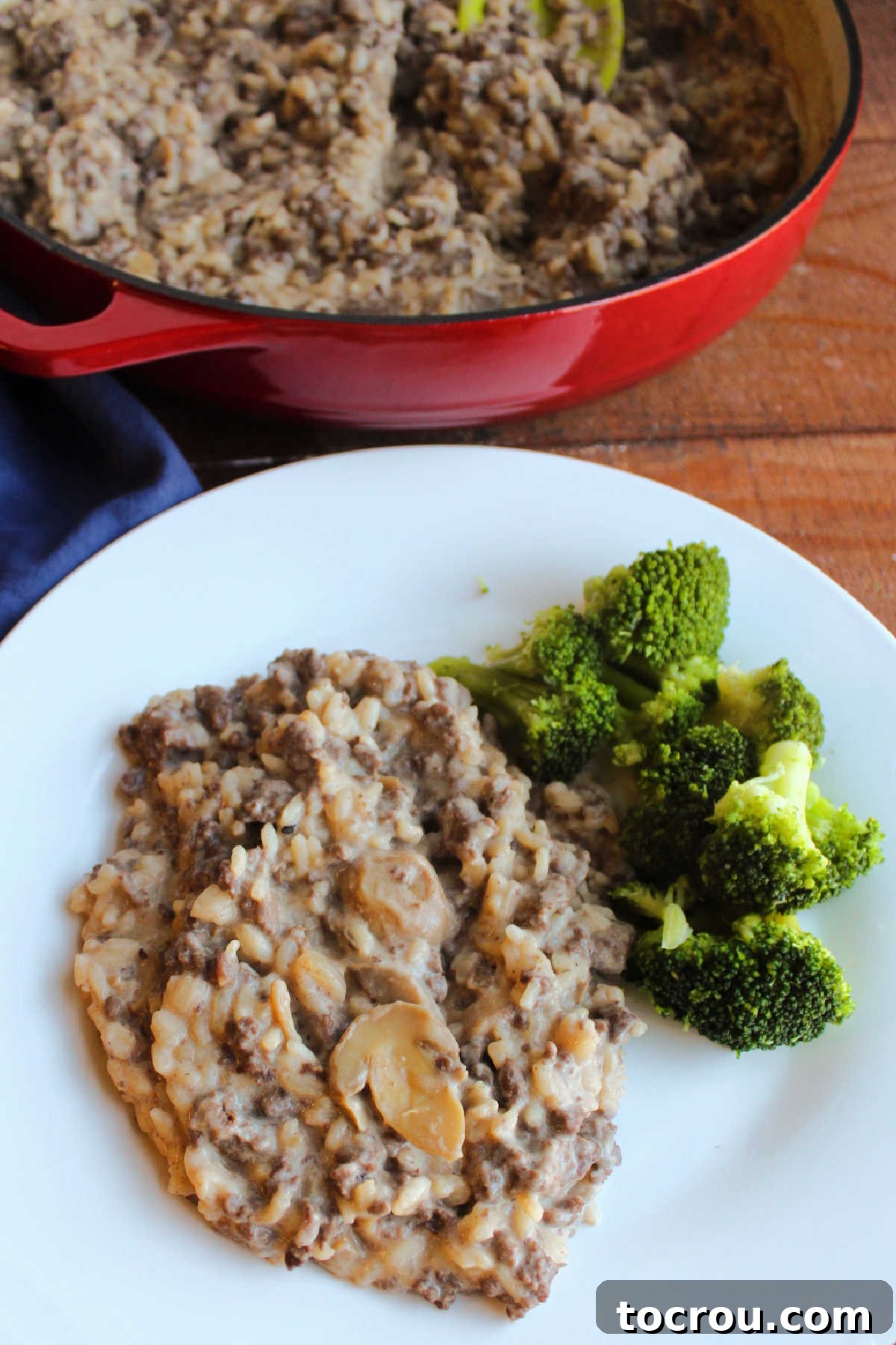 Hearty Creamy Venison Mushroom Rice 8 Dinner plate with creamy rice mixture and steamed broccoli with the cast iron pan containing the rest of the rice mixture in the background.