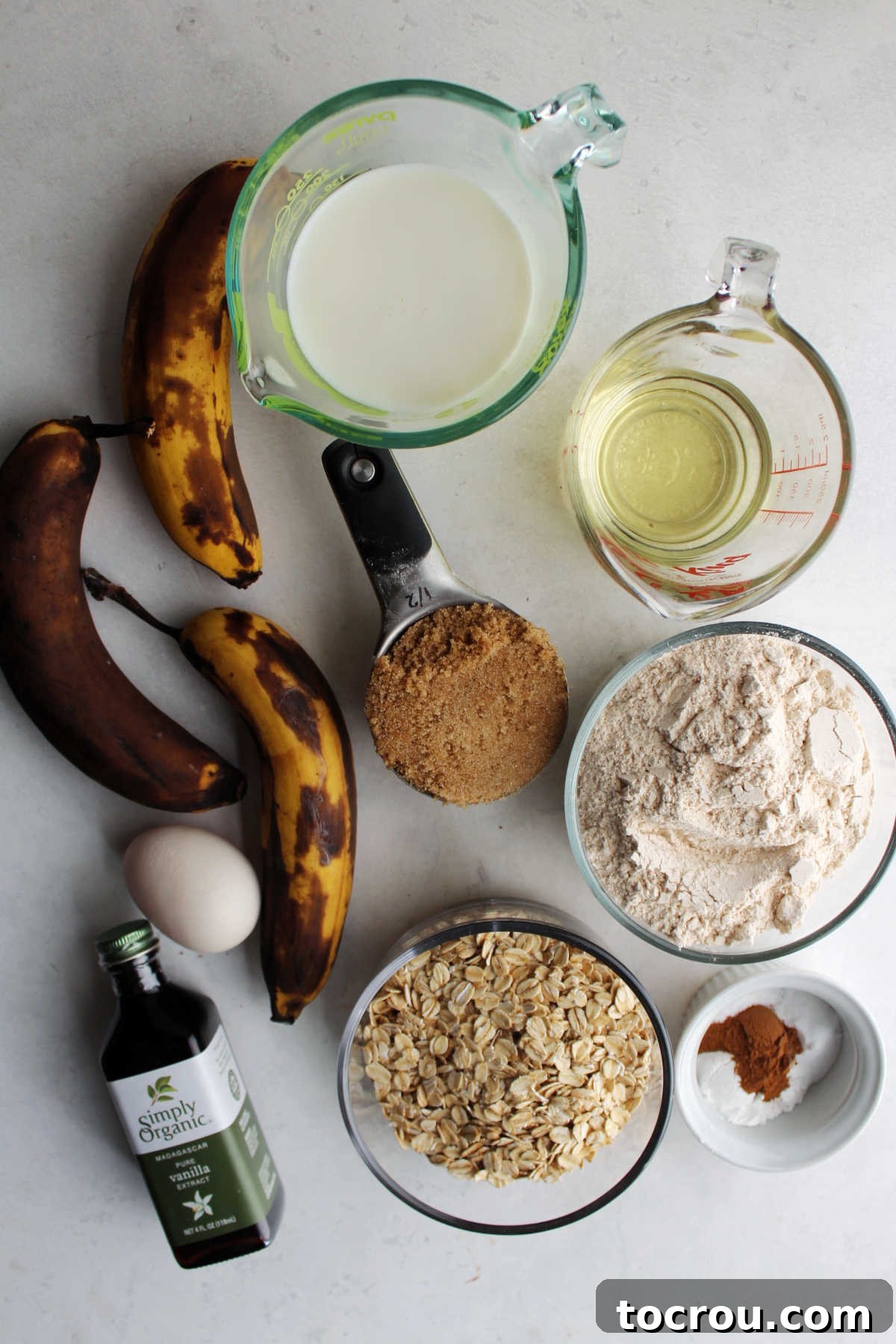 Ingredients for banana oat muffins including ripe bananas, oatmeal, flour, brown sugar, milk, oil, egg, vanilla, cinnamon, baking soda, and baking powder.