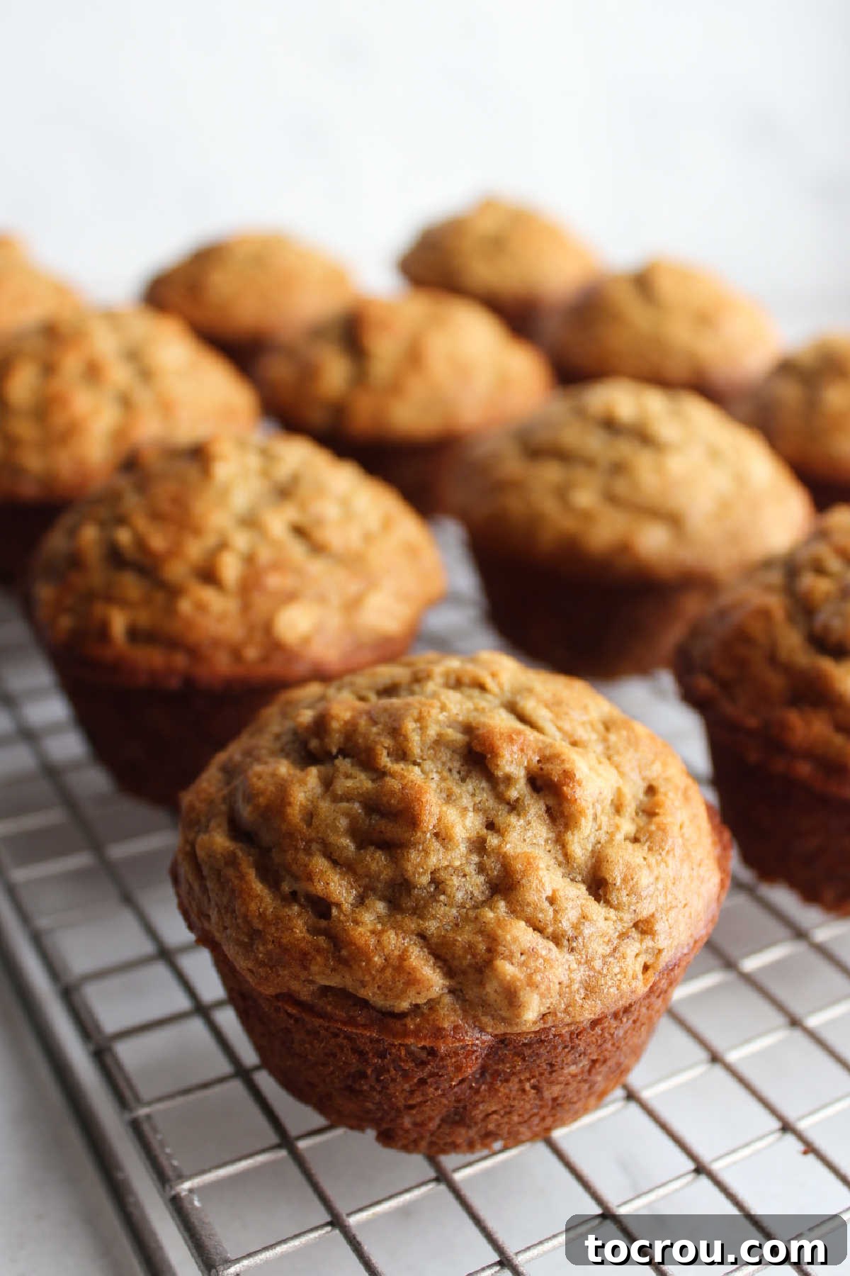 A wire cooling rack filled with a fresh batch of golden banana muffins with oats, cooling down after baking.
