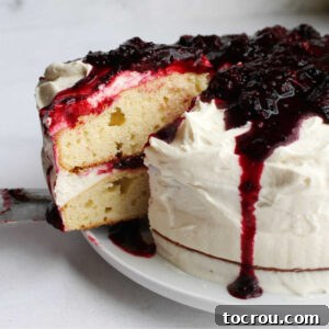 Lifting first slice of blackberry shortcake cake out showing two layers of dense cake with fluffy white ermine frosting and blackberry sauce.