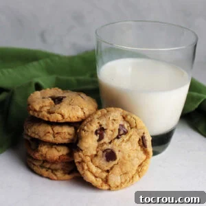 Stack of freshly baked brown butter cowgirl cookies with chocolate chips and oatmeal next to cup of milk.